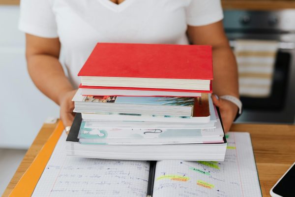 Close-up of a person holding a stack of colorful books over an open notebook.